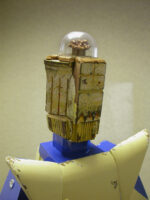 Close-up of the wooden head of a robot which contains a nut within a transparent little dome