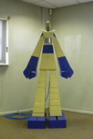 Front view of a sculpture of a blue and yellow robot made of wood