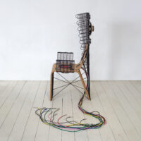 A bamboo chair adorned with black fridge coils, incorporating speakers and an intricate network of cables connected to them, meticulously designed for a mute sound experience.