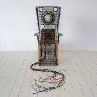 Back view of a bamboo chair adorned with black fridge coils, incorporating speakers and an intricate network of a various colours of cables connected to them.