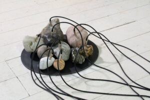 Stones of different shapes placed on a thin steel disc, properly prepared with audio jacks and connected with black audio cables.